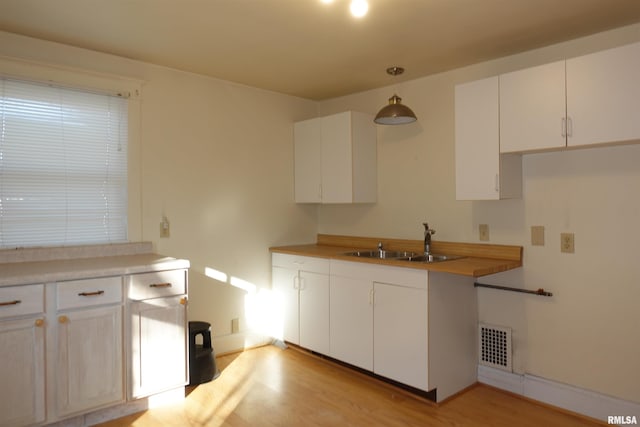 kitchen with light wood-type flooring, white cabinetry, sink, and decorative light fixtures