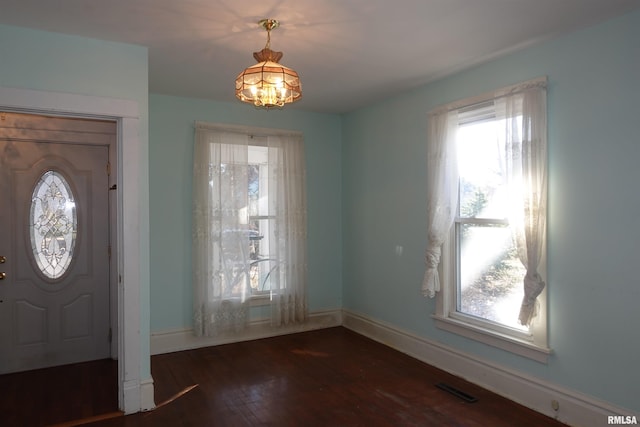 foyer entrance featuring dark hardwood / wood-style flooring, a wealth of natural light, and an inviting chandelier