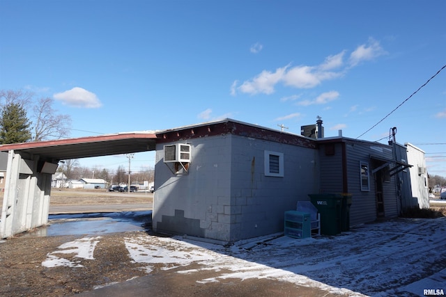 snow covered property with a carport and a wall mounted air conditioner