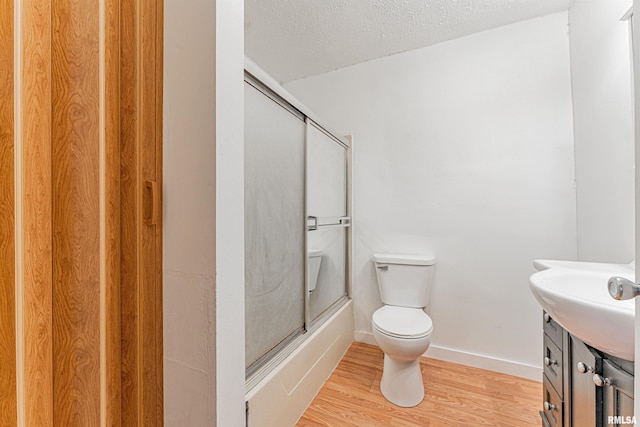 full bathroom featuring a textured ceiling, wood-type flooring, sink, toilet, and combined bath / shower with glass door