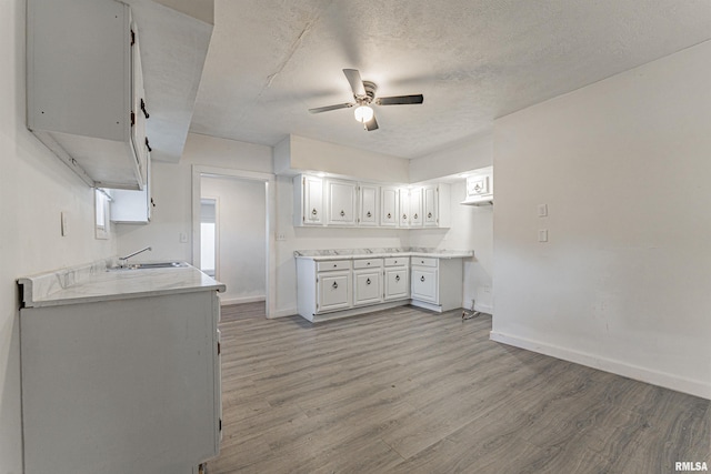 kitchen with a textured ceiling, white cabinetry, sink, ceiling fan, and light hardwood / wood-style flooring