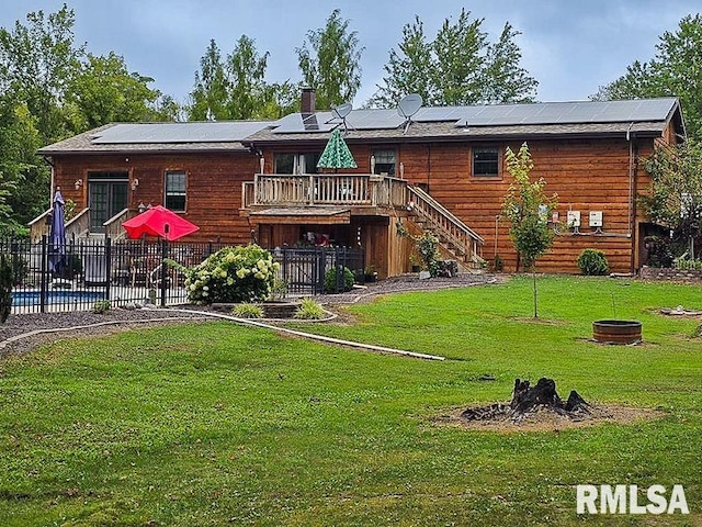 back of property with a wooden deck, an outdoor fire pit, a lawn, and solar panels