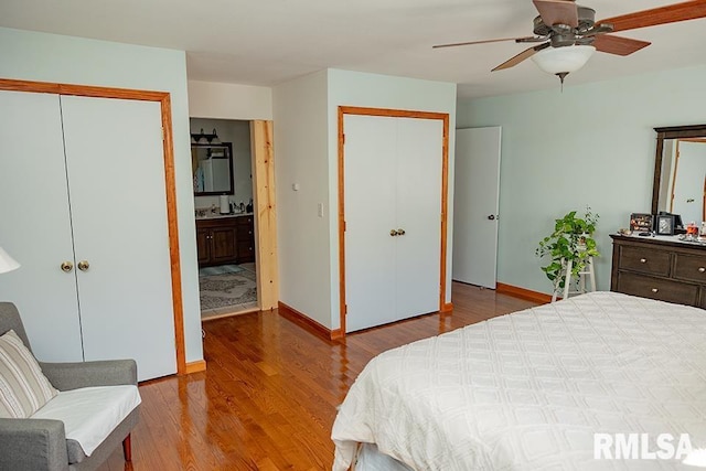 bedroom featuring ceiling fan, hardwood / wood-style flooring, connected bathroom, and two closets