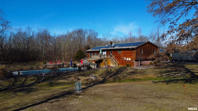 rear view of house with a wooden deck, a yard, and solar panels