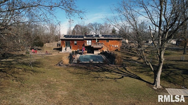 back of property featuring a wooden deck, a lawn, a patio, and solar panels