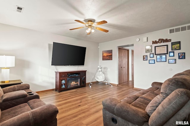 living room with ceiling fan, a textured ceiling, and light hardwood / wood-style flooring