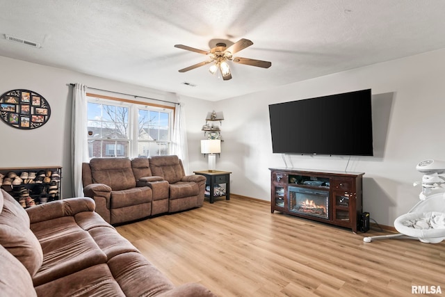 living room featuring ceiling fan, a textured ceiling, and light wood-type flooring