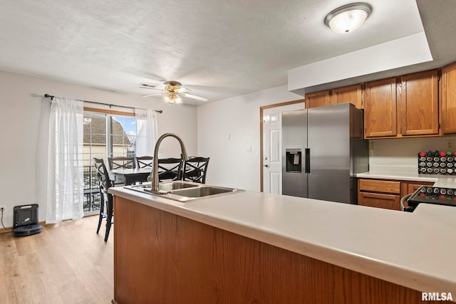 kitchen with sink, light hardwood / wood-style flooring, ceiling fan, stainless steel refrigerator with ice dispenser, and kitchen peninsula