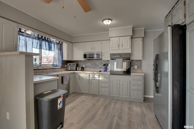 kitchen with appliances with stainless steel finishes, decorative backsplash, sink, light wood-type flooring, and ceiling fan