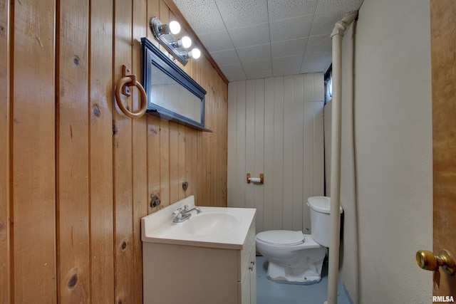 bathroom with toilet, wood walls, and vanity