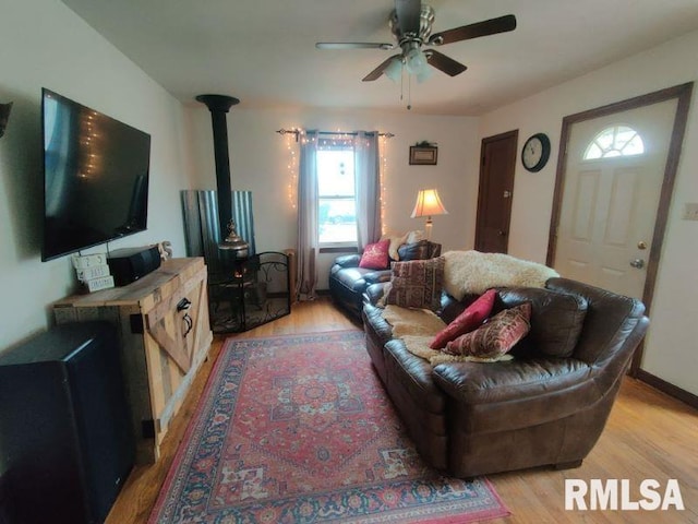 living room with ceiling fan, a wood stove, and light hardwood / wood-style flooring