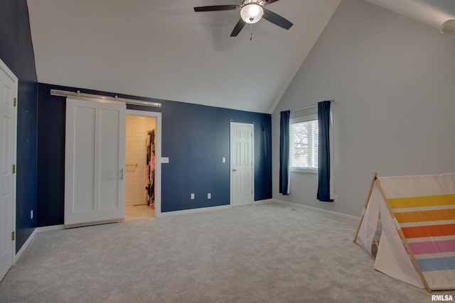 unfurnished bedroom featuring a barn door, high vaulted ceiling, light colored carpet, and ceiling fan