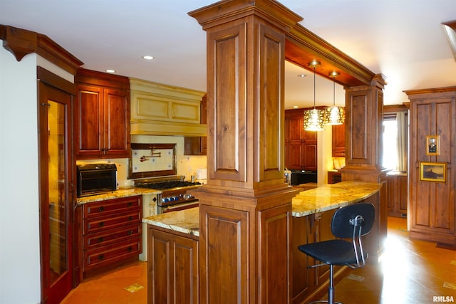 kitchen with hanging light fixtures, stainless steel stove, a center island, a breakfast bar, and decorative columns