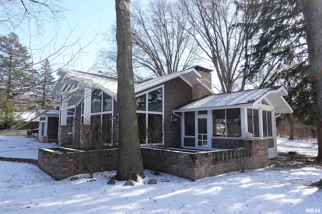 snow covered rear of property with a sunroom