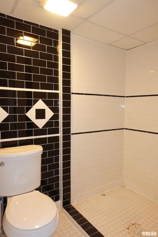 bathroom featuring toilet, tile walls, a tile shower, tile patterned floors, and a paneled ceiling