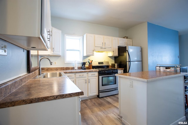 kitchen featuring white cabinets, appliances with stainless steel finishes, a kitchen island, sink, and light wood-type flooring