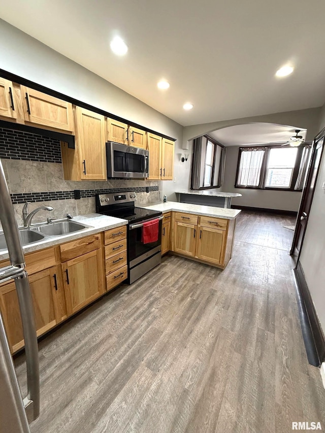 kitchen with hardwood / wood-style floors, tasteful backsplash, sink, kitchen peninsula, and stainless steel appliances