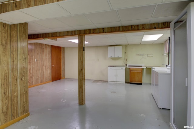 basement with a paneled ceiling, wooden walls, and sink