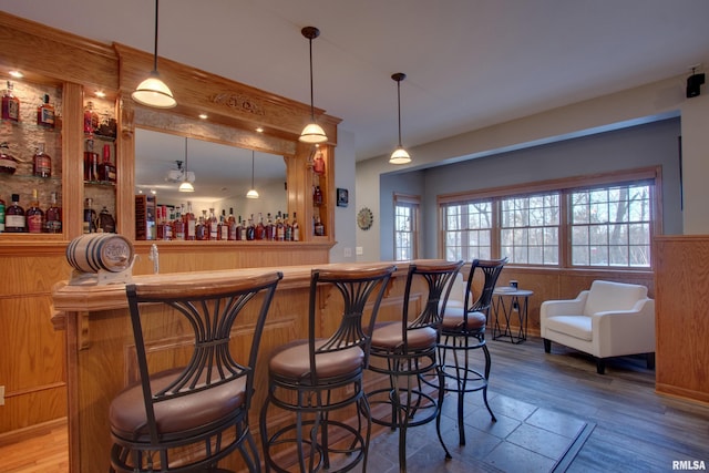 bar featuring wood-type flooring, decorative light fixtures, and wooden walls