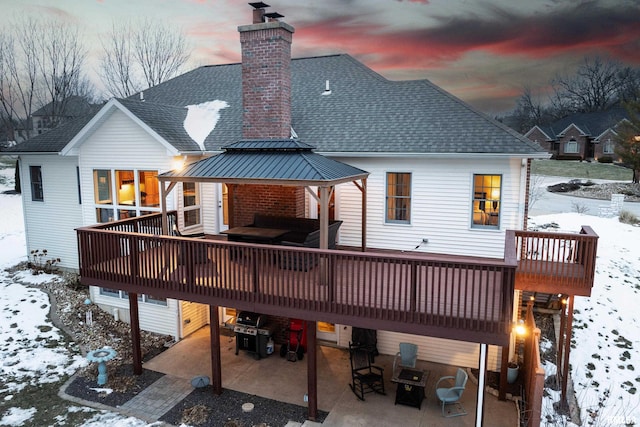 snow covered rear of property featuring a patio area and a deck