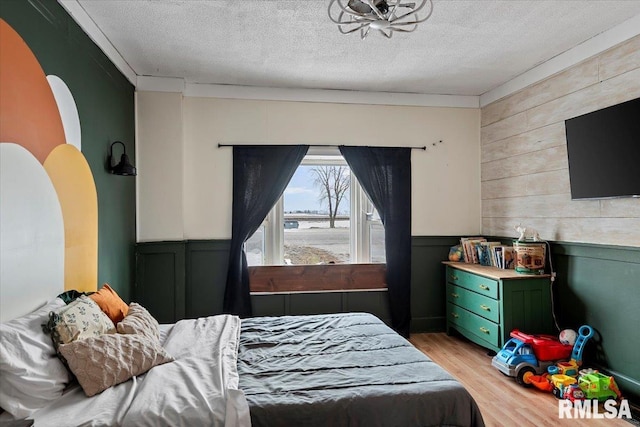 bedroom with light wood-type flooring, wood walls, and a textured ceiling