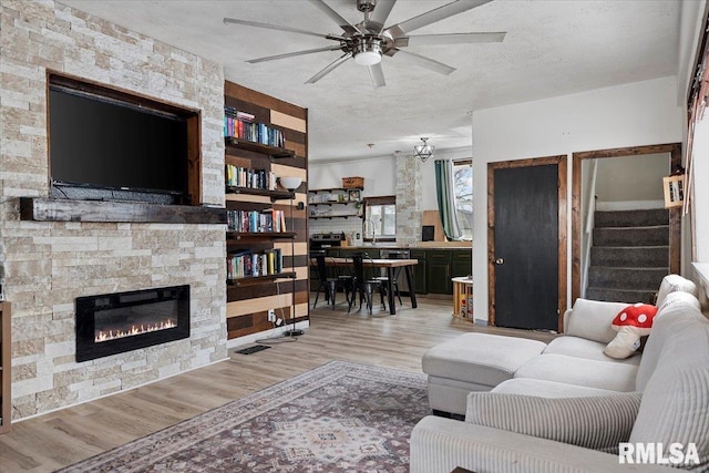 living room featuring light hardwood / wood-style floors, ceiling fan, a textured ceiling, and a stone fireplace