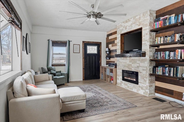 living room featuring a healthy amount of sunlight, a textured ceiling, light hardwood / wood-style flooring, and a stone fireplace