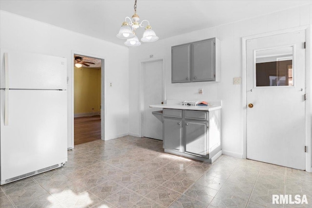 kitchen with white refrigerator, ceiling fan with notable chandelier, gray cabinetry, and pendant lighting