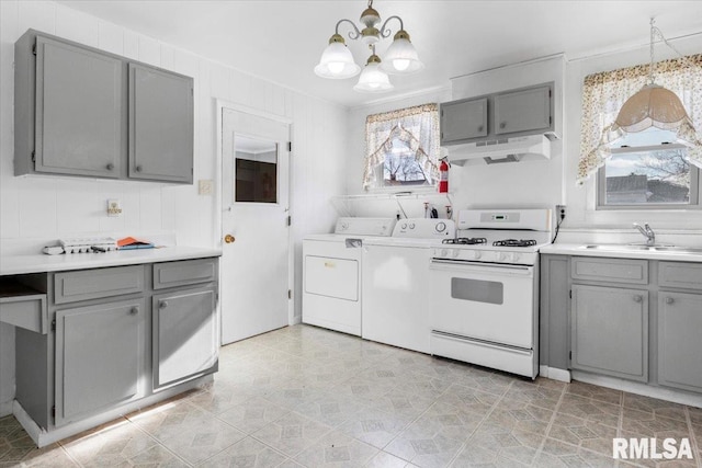 kitchen with white gas range, sink, washer and clothes dryer, and decorative light fixtures