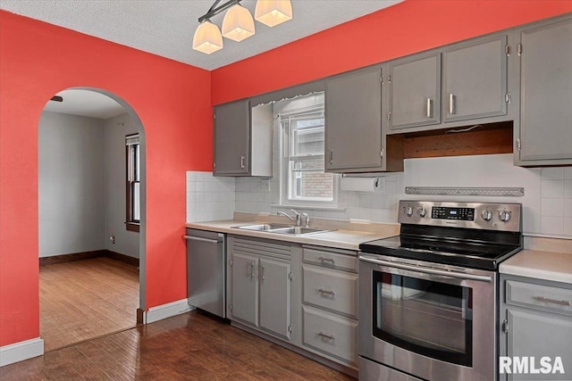 kitchen with sink, dark wood-type flooring, gray cabinets, backsplash, and stainless steel appliances