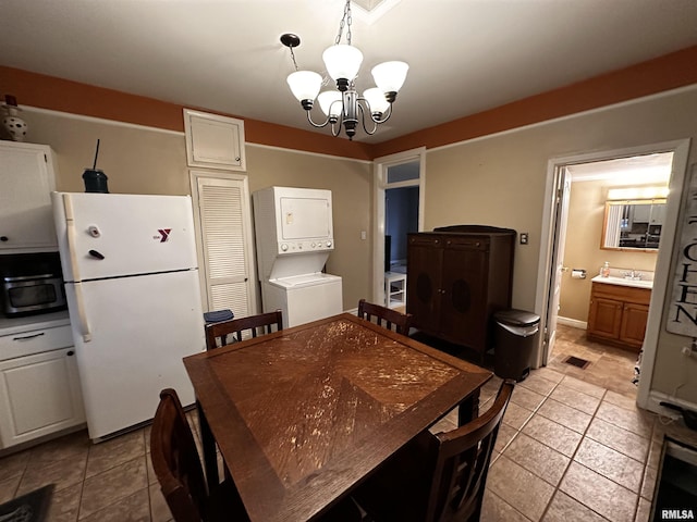 tiled dining room featuring sink, a chandelier, and stacked washer / dryer