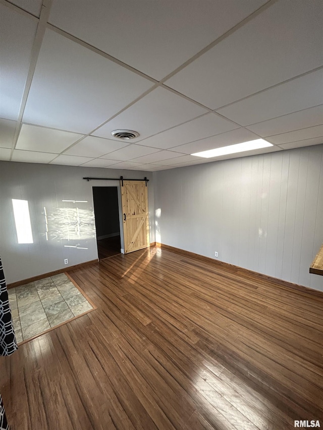 basement featuring wood-type flooring, a barn door, and a drop ceiling