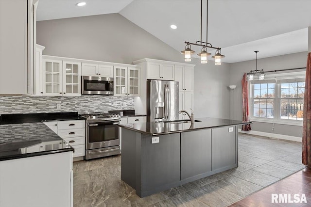 kitchen featuring appliances with stainless steel finishes, pendant lighting, an island with sink, white cabinets, and backsplash