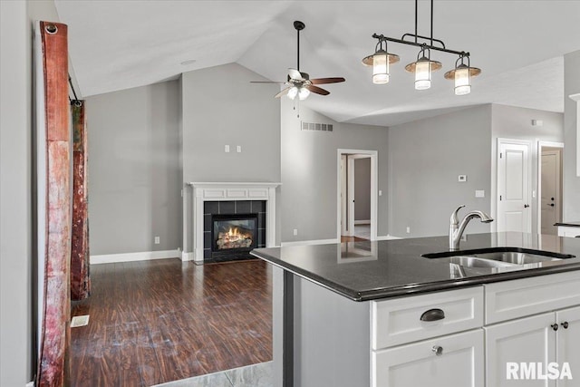 kitchen featuring white cabinetry, lofted ceiling, sink, a tiled fireplace, and a center island with sink