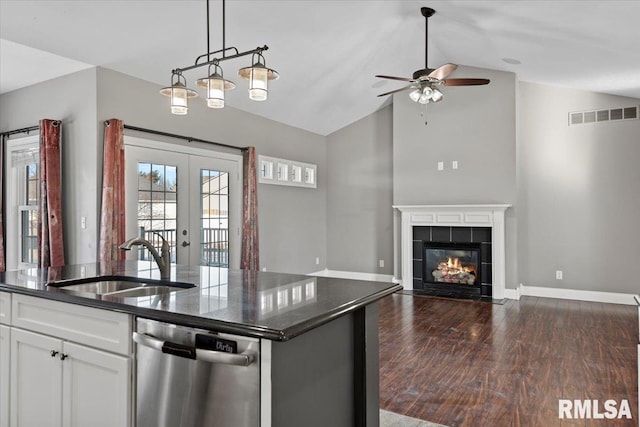 kitchen featuring sink, vaulted ceiling, dishwasher, a tile fireplace, and white cabinets