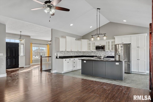 kitchen featuring backsplash, hanging light fixtures, stainless steel appliances, white cabinets, and a center island with sink