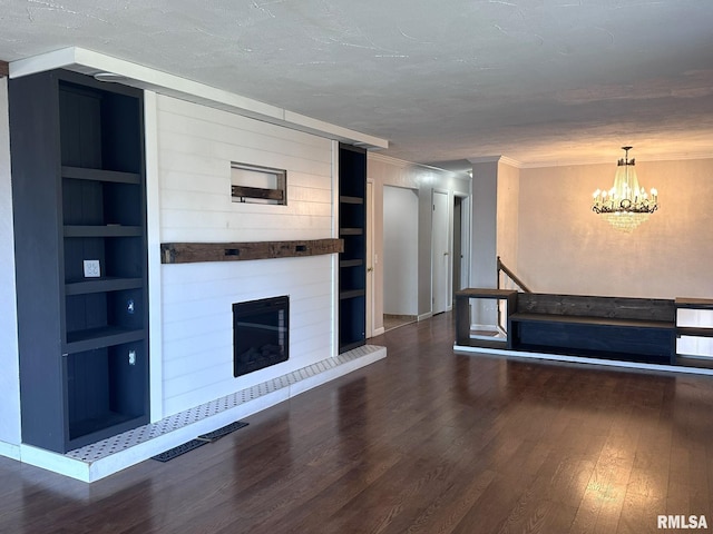 unfurnished living room featuring an inviting chandelier, a textured ceiling, a large fireplace, dark hardwood / wood-style floors, and built in features