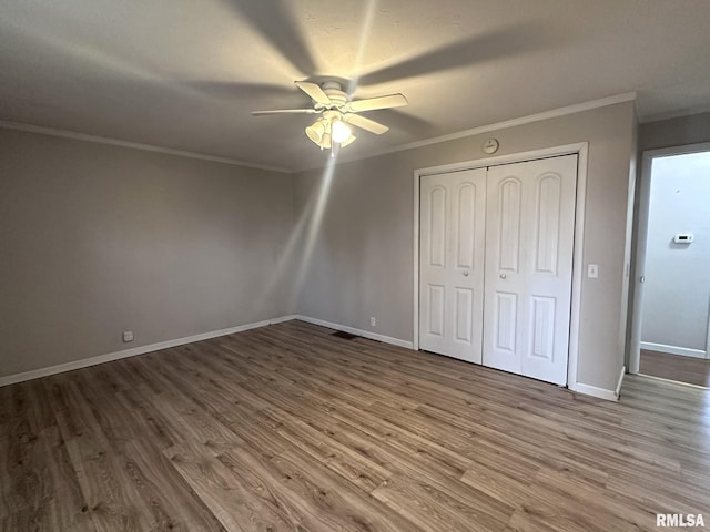 unfurnished bedroom featuring hardwood / wood-style flooring, crown molding, ceiling fan, and a closet