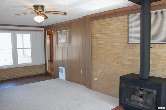 interior space featuring ceiling fan, ornamental molding, brick wall, and a wood stove