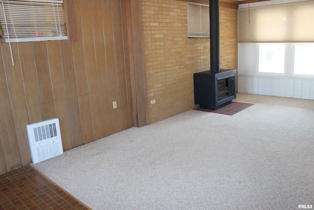 unfurnished living room featuring wood walls, carpet flooring, and a wood stove