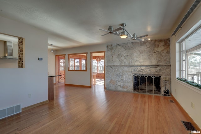 unfurnished living room with ceiling fan, a stone fireplace, hardwood / wood-style floors, and a wealth of natural light