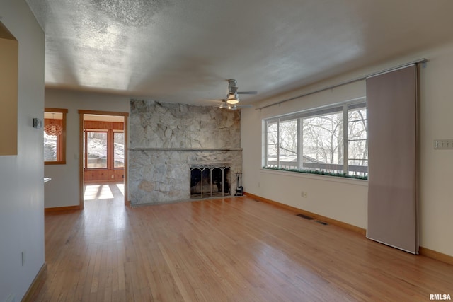 unfurnished living room with ceiling fan, a fireplace, light wood-type flooring, and a wealth of natural light