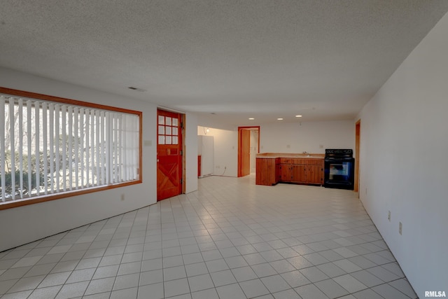 unfurnished living room with sink, a textured ceiling, and light tile patterned floors