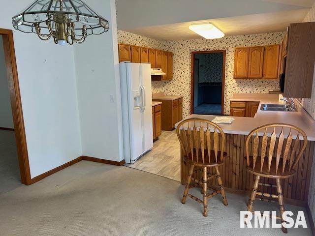 kitchen with sink, hanging light fixtures, a notable chandelier, white refrigerator with ice dispenser, and kitchen peninsula