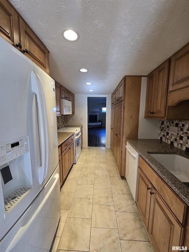 kitchen featuring dark stone countertops, decorative backsplash, light tile patterned floors, white appliances, and a textured ceiling