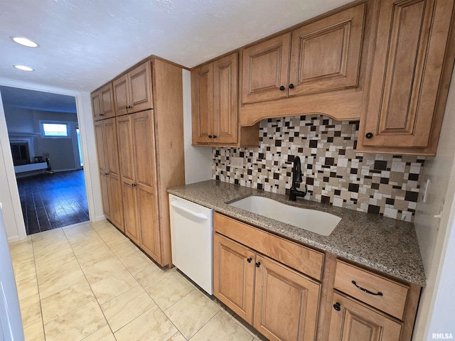 kitchen with light tile patterned flooring, sink, backsplash, dark stone counters, and white dishwasher