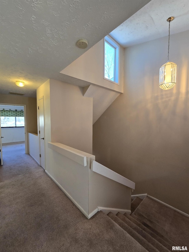 stairs featuring vaulted ceiling, plenty of natural light, carpet floors, and a textured ceiling