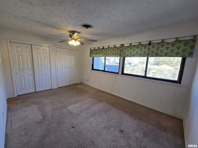 unfurnished bedroom with carpet floors, two closets, a textured ceiling, and ceiling fan