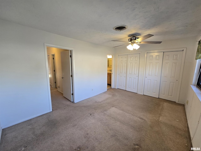 unfurnished bedroom featuring two closets, light carpet, a textured ceiling, and ceiling fan