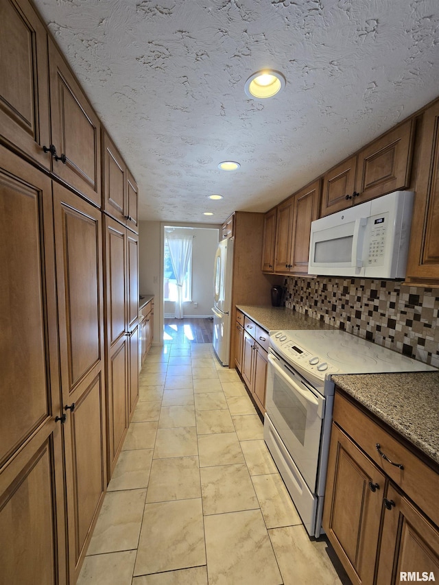 kitchen with tasteful backsplash, light tile patterned floors, white appliances, and light stone counters